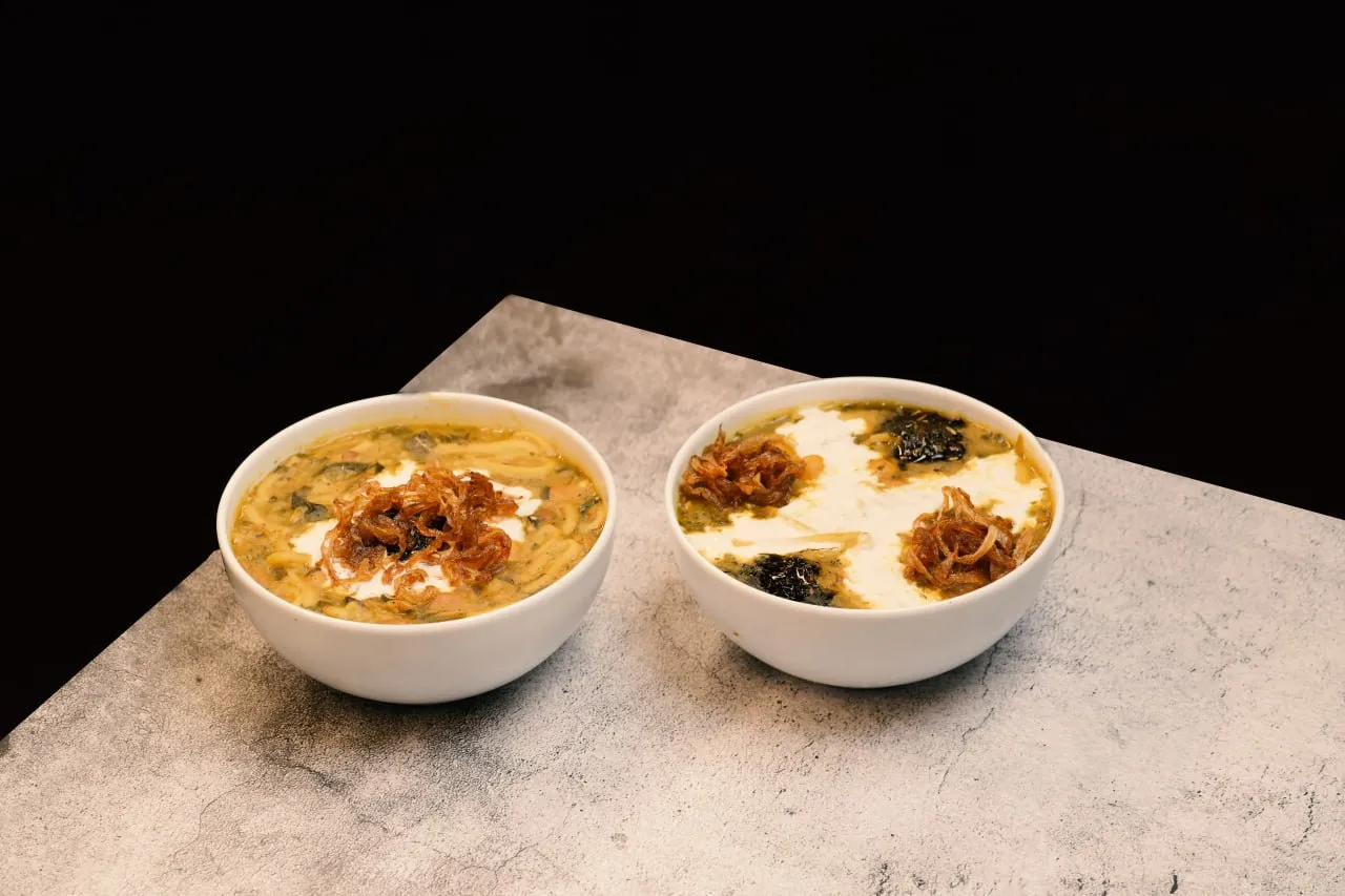 Two bowls of Persian herb noodle soup topped with yoghurt and fried onions
