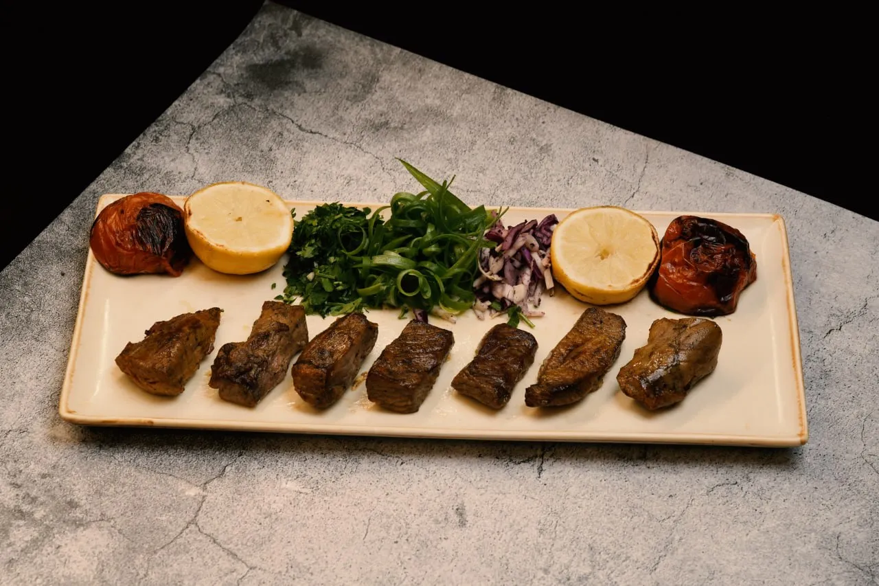 Beef skewers served with herbs, lemon and grilled tomato