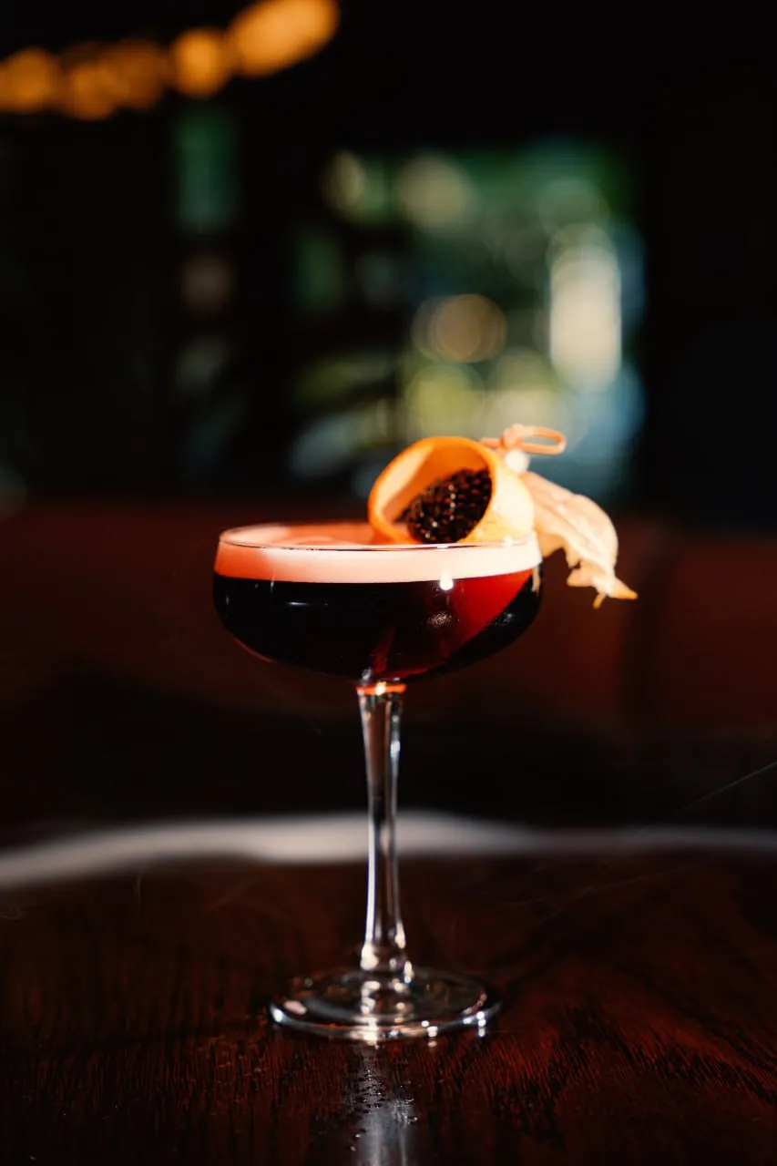 A deep red coupe cocktail with a citrus and berry garnish