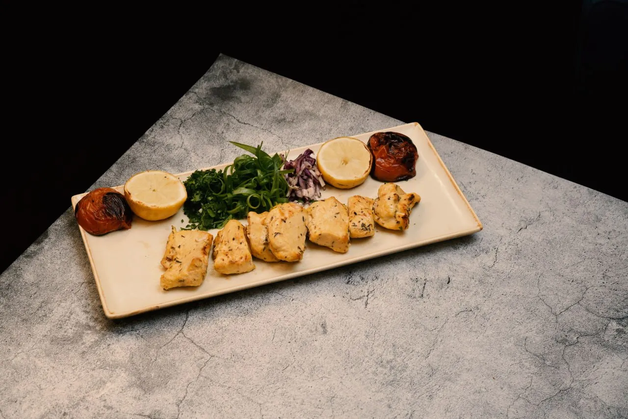 Chicken skewers served with herbs, lemon and grilled tomato