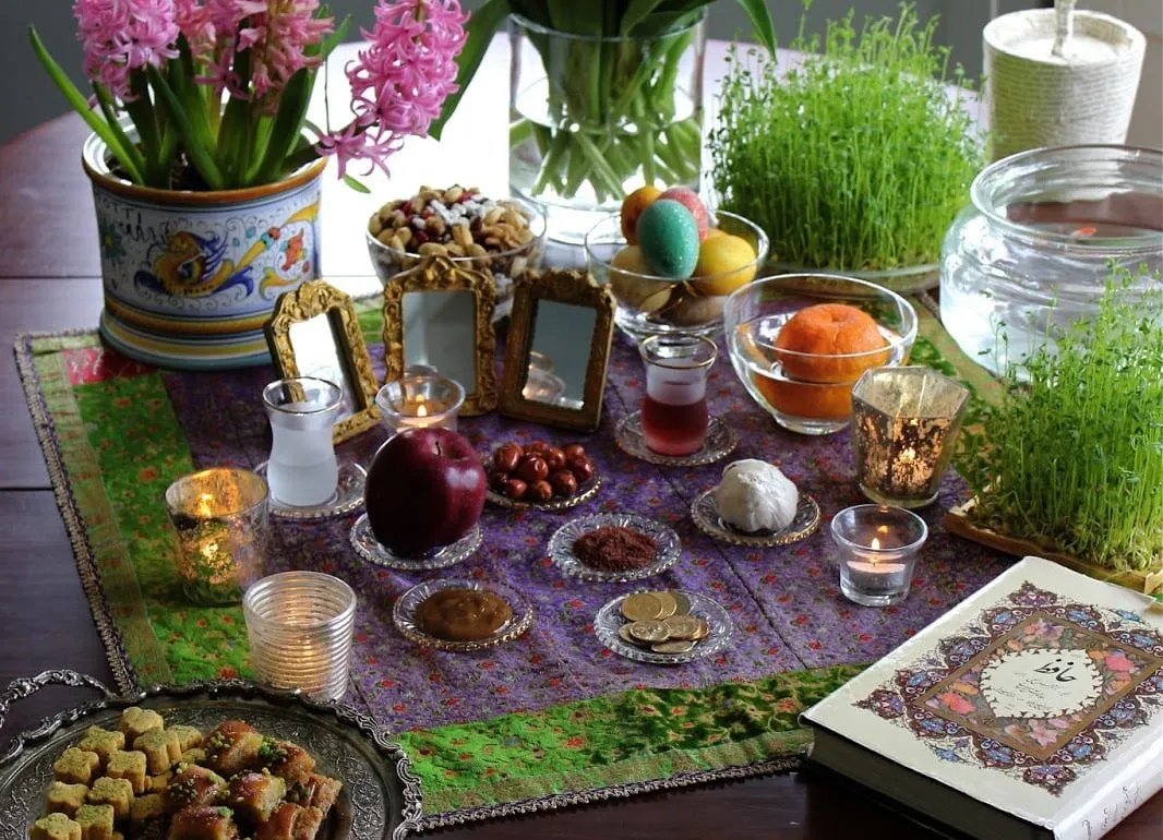 A Nowruz table with sabzeh, candles, fruit, flowers and a book of Hafez