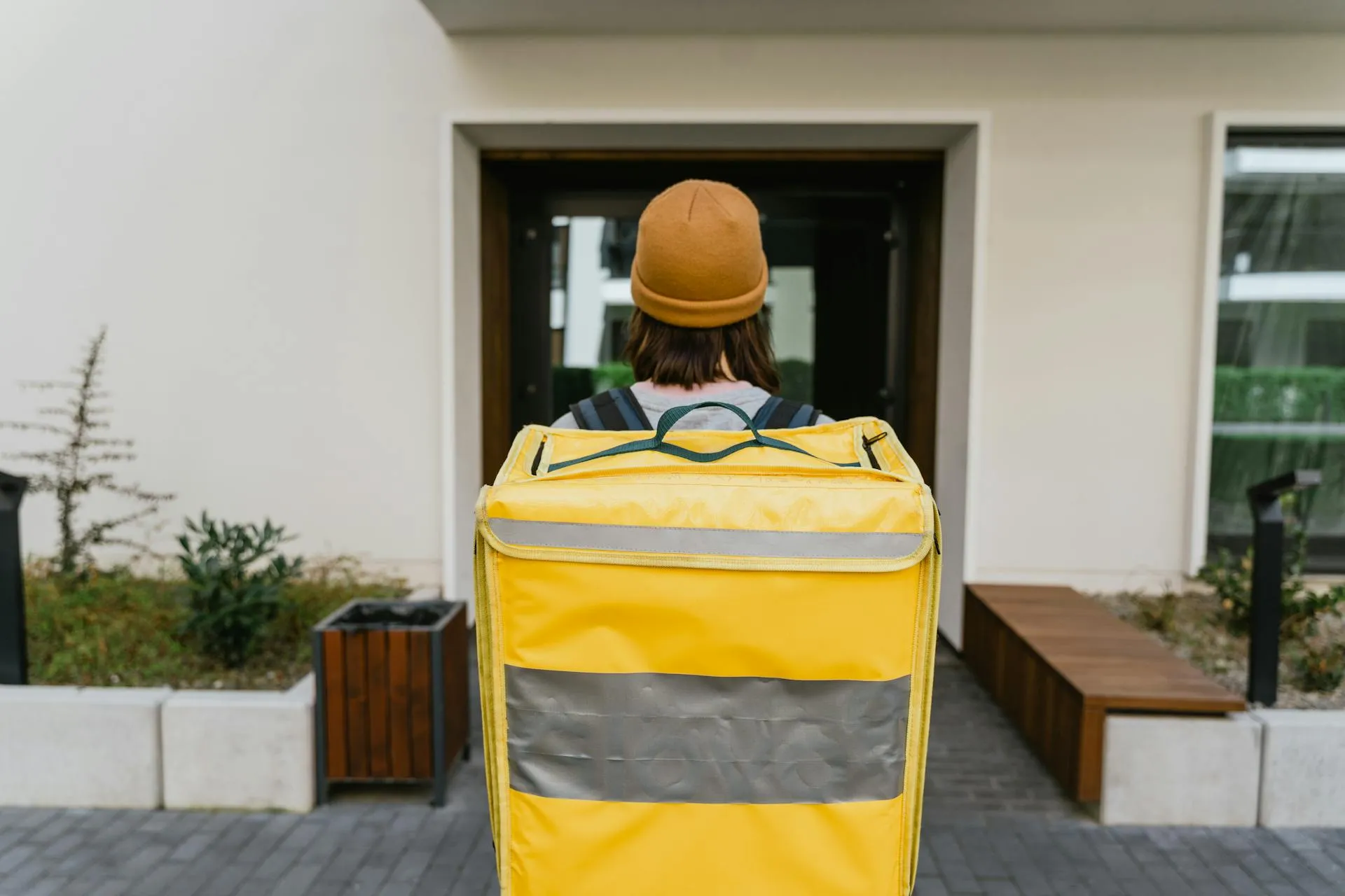 A courier carrying a yellow delivery bag outside a front door