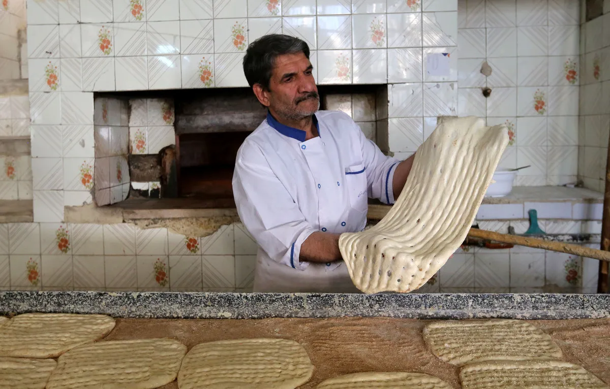 A baker stretching fresh Persian bread in front of an oven