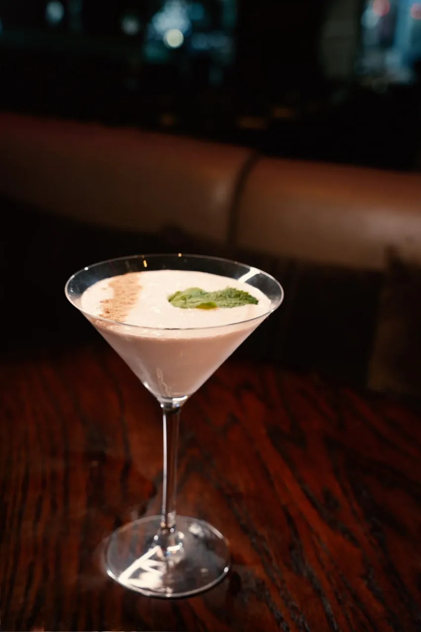 A pale pink martini served on a polished wooden table