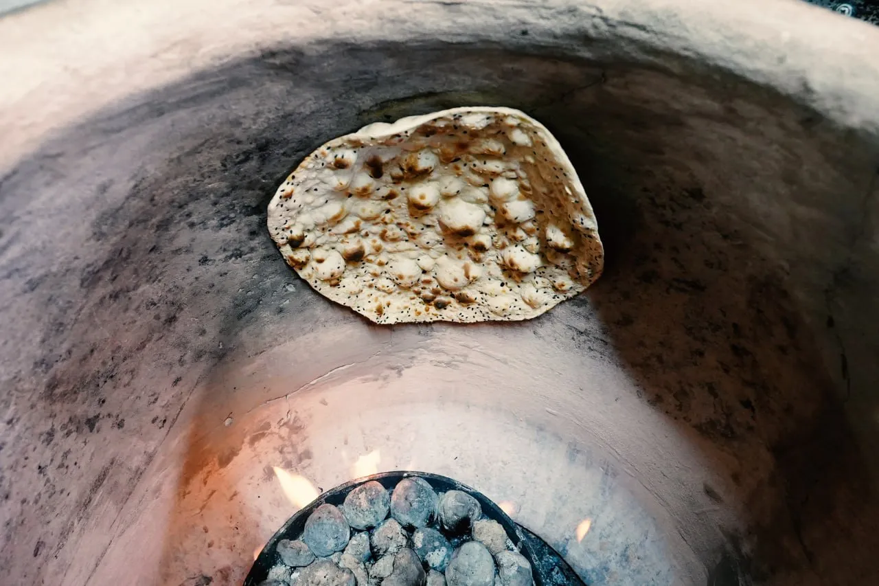 Persian bread baking against the wall of a clay tandoor oven